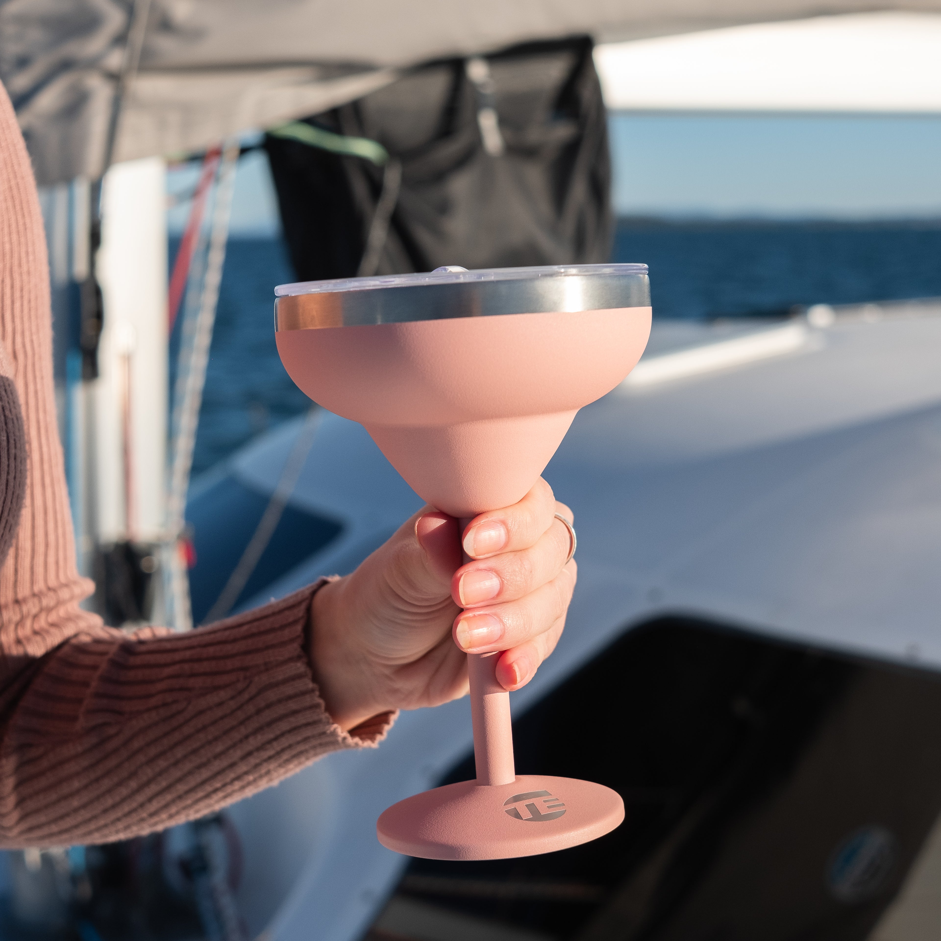 Person holding a pink cocktail glass on a boat