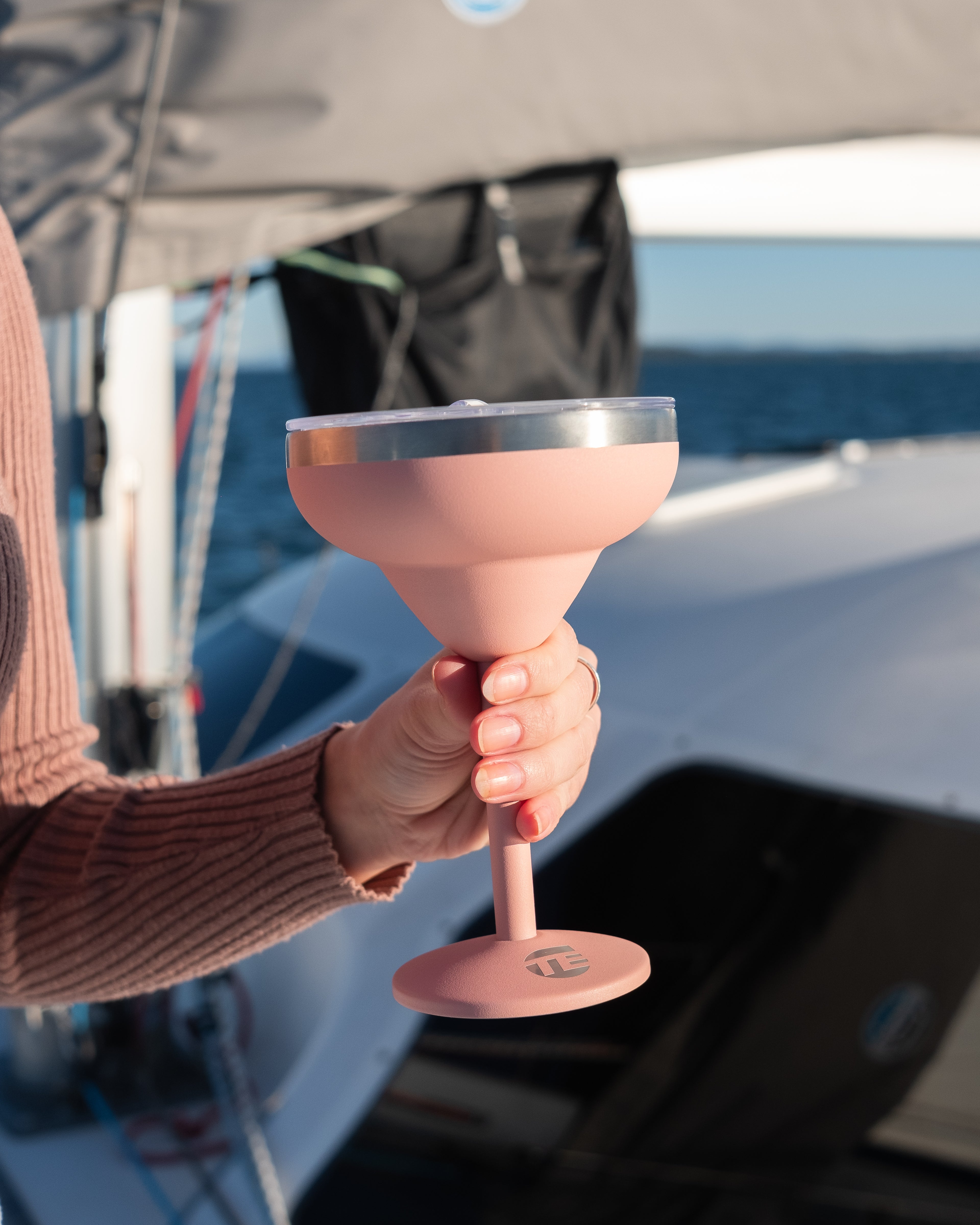 Person holding a pink cocktail glass on a boat