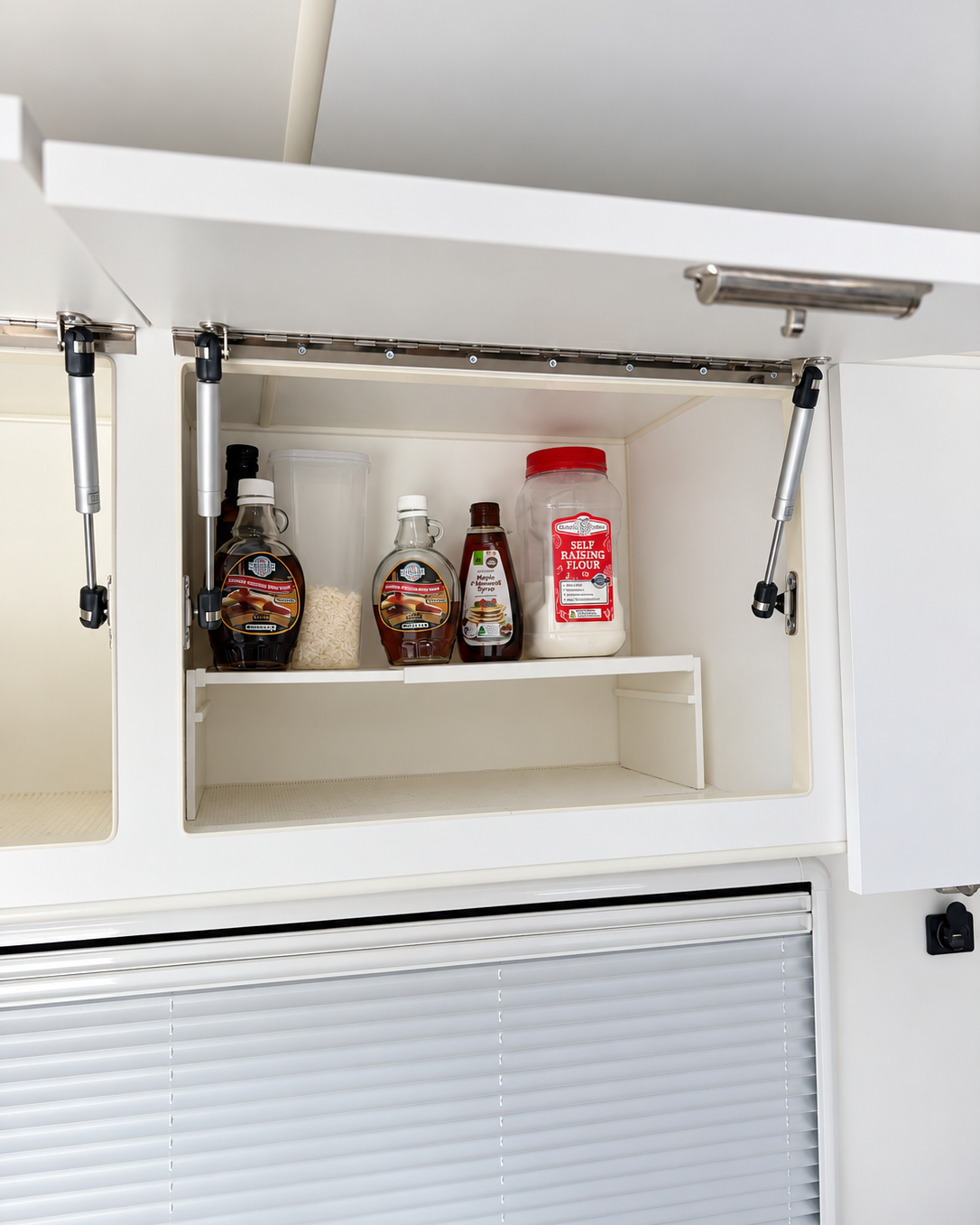 white extendable plastic shelf with items on top in a caravan cupboard to maximise space
