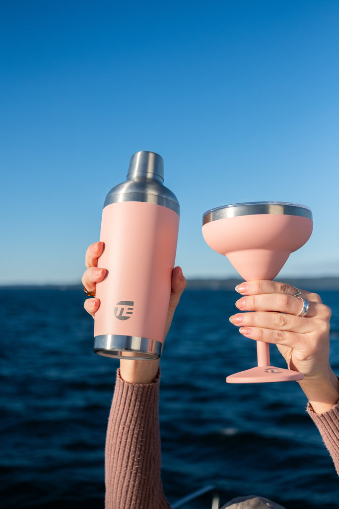 Two pink drink insulated drink ware items held against a blue sky and ocean background