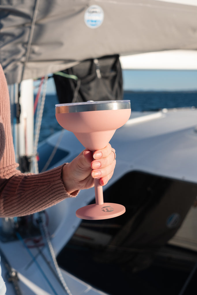 Person holding a pink cocktail glass on a boat