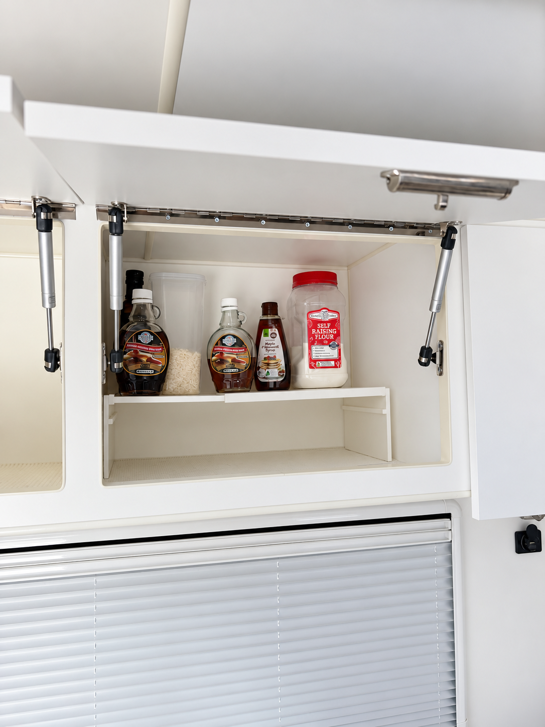 white extendable plastic shelf with items on top in a caravan cupboard to maximise space